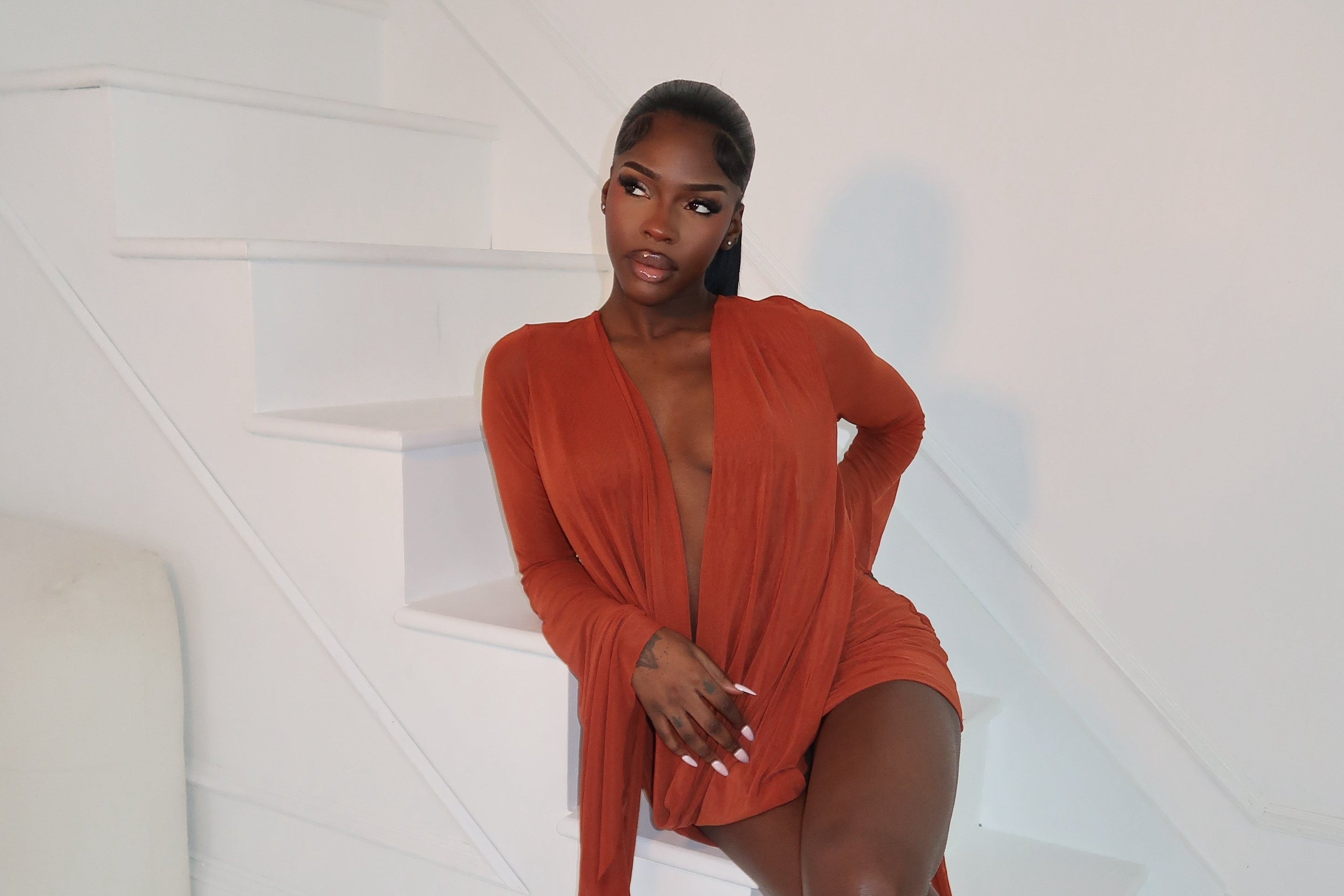 Woman in a red dress sitting on a white chair against a white background